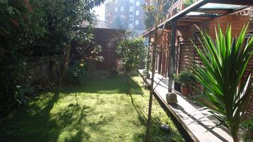 A small, well-maintained garden with a wooden deck, various potted plants, and a brick wall.