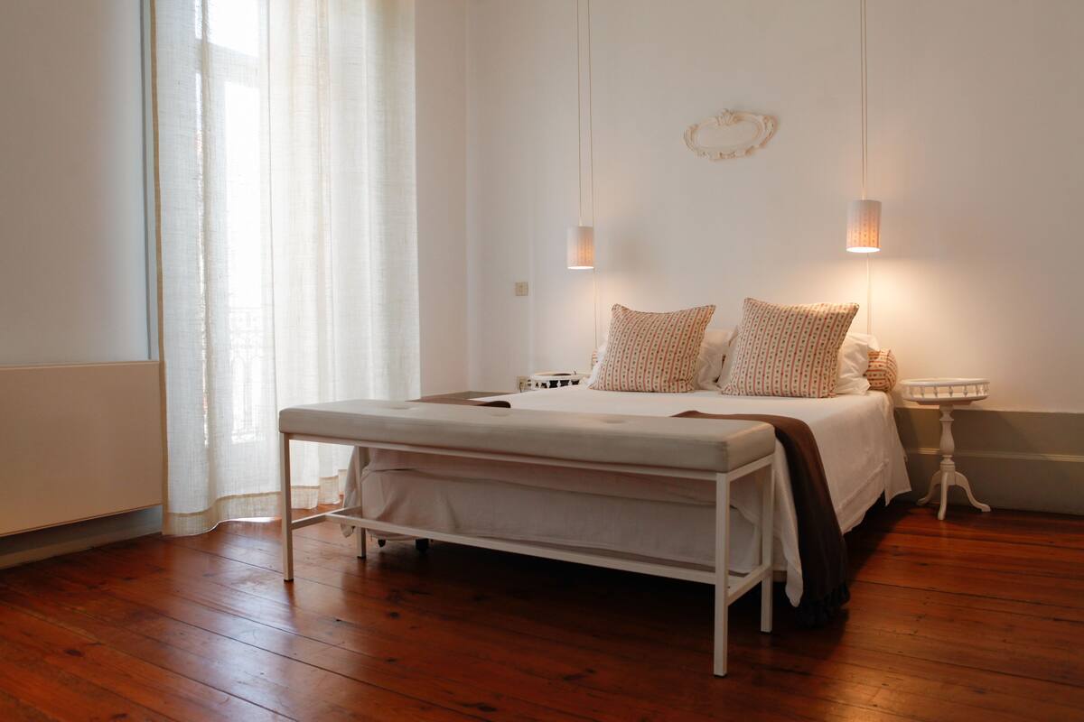 Un dormitorio con cama, mesitas de noche y una ventana con cortinas.