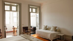 A bedroom with a bed, a bench, and a small table. There is a door leading to another room with a chair and a table. - Pensão Favorita (Porto)