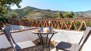A terrace with a table set for two, two chairs, and a view of a hilly landscape.
