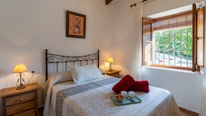 Een slaapkamer met een bed, twee nachtkastjes, een raam met zonwering en een ingelijst kunstwerk aan de muur.