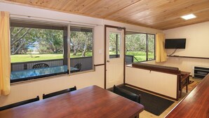 A room with a wooden ceiling, large windows, a TV mounted on the wall, and a table with chairs. - Siesta Park Holiday Resort (Busselton)