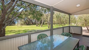 A covered outdoor area with a glass table and chairs, overlooking a grassy landscape with trees. - Siesta Park Holiday Resort (Busselton)