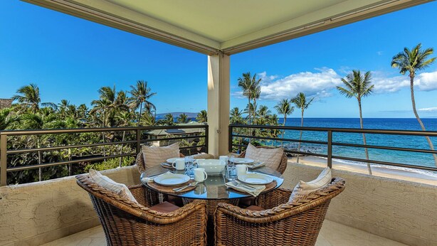 A covered outdoor dining area with a view of the ocean and palm trees.