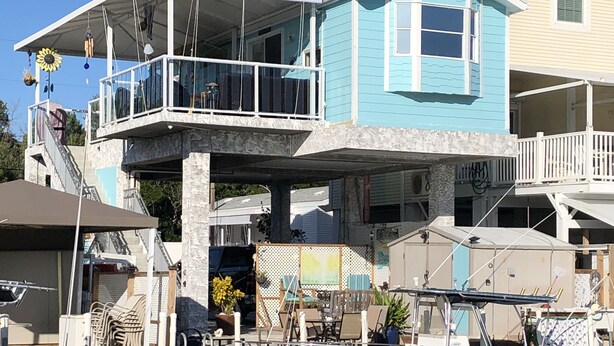 A waterfront property with a multi-level house, a dock with a boat, and outdoor furniture. - *Snowbirds Paradise* (Marathon)