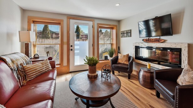 A living room with a fireplace, leather sofas, a coffee table, and a TV mounted on the wall.