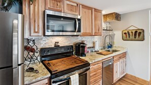 A modern kitchen with wooden cabinets, stainless steel appliances, a granite countertop, and a decorative wall piece.