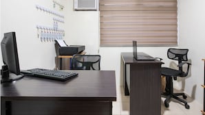 A small office with a desk, computer, and chair. There is an air conditioning unit and a window with blinds. - OYO 474 Nizami Condotel (Mandaluyong)