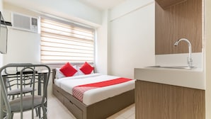 A bedroom with a bed, a desk, a chair, a window with blinds, a sink, and a ceiling light. - OYO 474 Nizami Condotel (Mandaluyong)