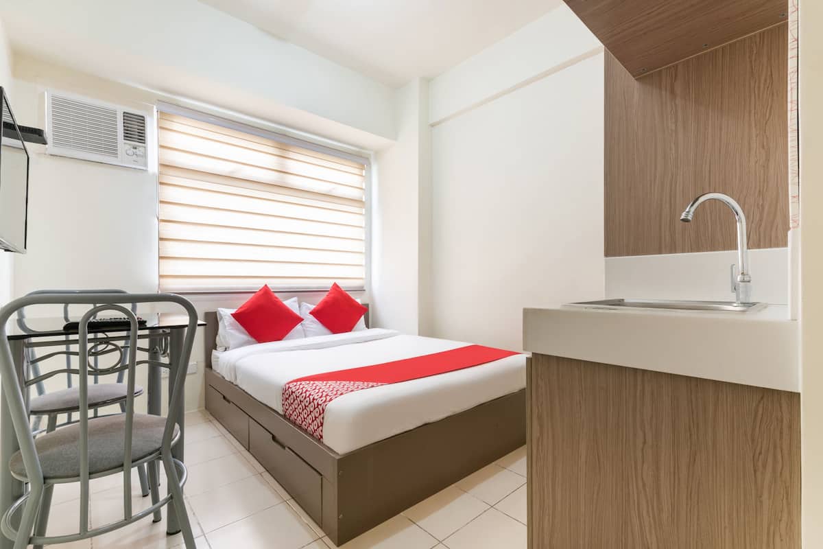 Un dormitorio con cama, escritorio, silla, ventana con persianas, lavamanos y una lámpara en el techo.