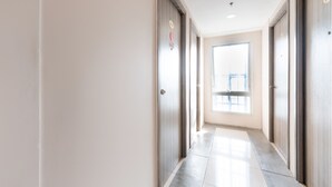 A corridor with a tiled floor, wooden doors, and a window at the end. - OYO 474 Nizami Condotel (Mandaluyong)