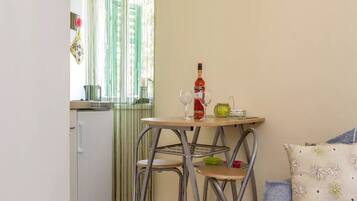 A small kitchenette with a refrigerator, a table with two chairs, and a window with vertical blinds.
