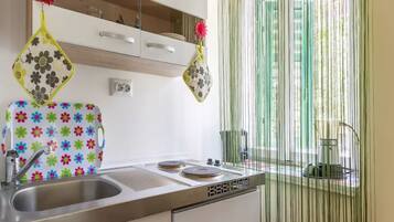 A kitchen with a stainless steel sink, a colorful backsplash, and a window with vertical blinds.