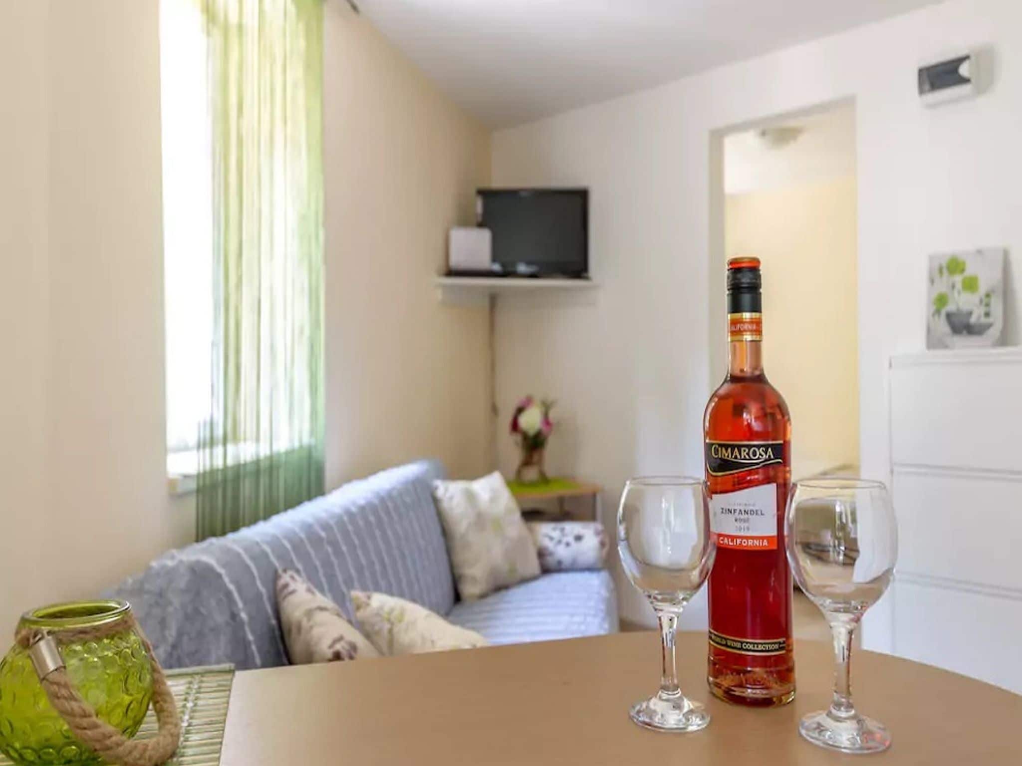 A living room with a sofa, a table with a bottle of Cimarosa wine and two glasses, and a television on a shelf.