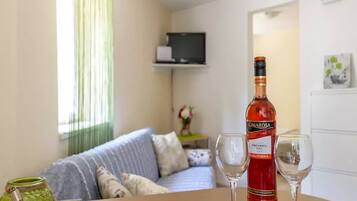 A living room with a sofa, a table with a bottle of Cimarosa wine and two glasses, and a television on a shelf.