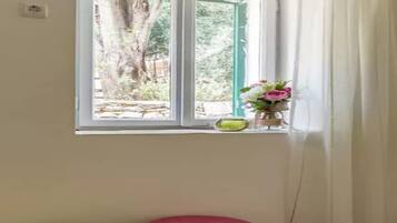 A room with a window, a green stool, a red stool, and a vase with flowers on the windowsill.