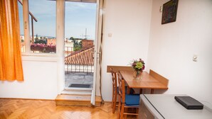 Una habitación con piso de madera en patrón de espiga, una mesa de comedor de madera con sillas, un refrigerador pequeño y una ventana con vistas a edificios y un balcón.