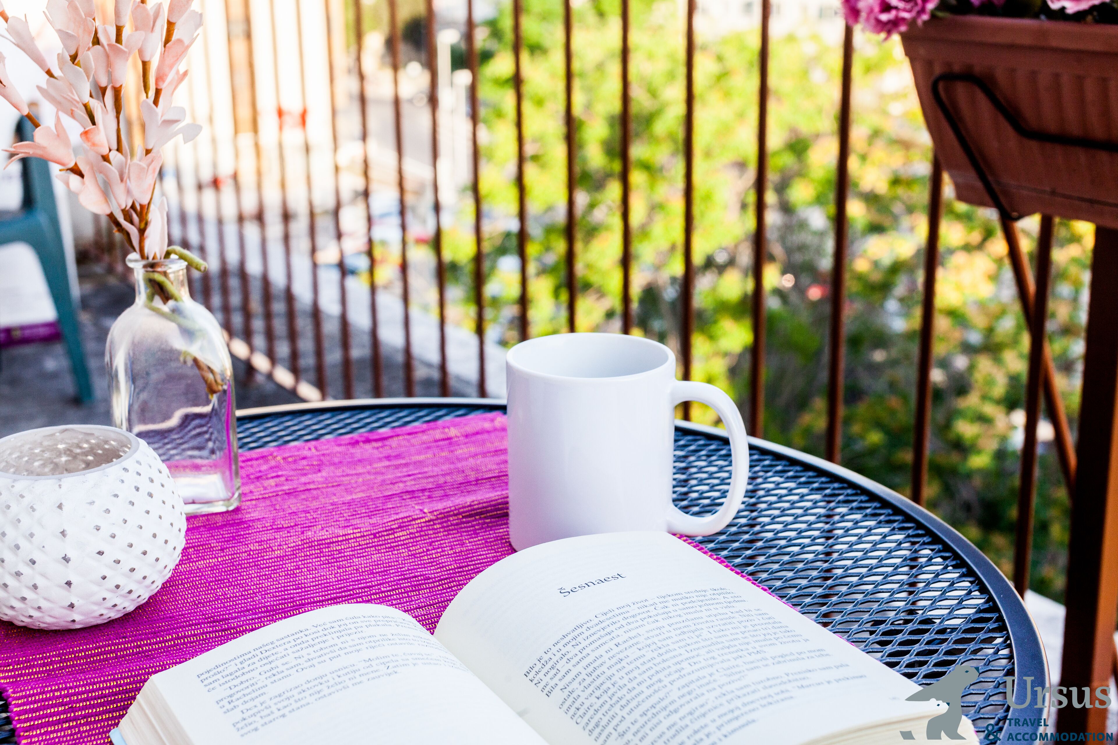 An open book on a table, a white mug, and a clear glass vase with flowers.