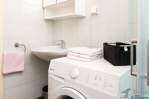 A modern bathroom with a washing machine, sink, and stacked towels. - Royal View Apartment (Split)