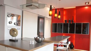 Een moderne keuken met een centraal eiland, witte barkrukken en rode accentmuren.