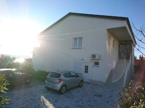 A two-story building with a white exterior, a small window, and a door. There is a car parked in front.