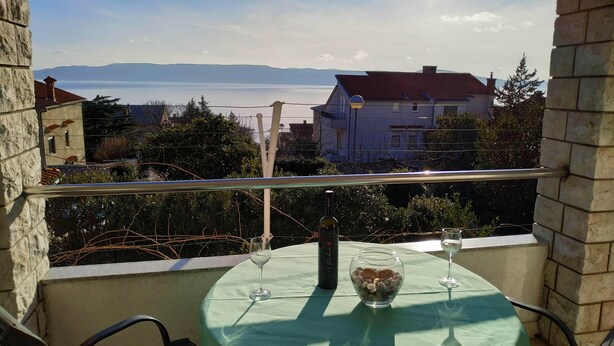 Een balkon met een tafel voor twee, met uitzicht op een prachtig waterlandschap en verre bergen.
