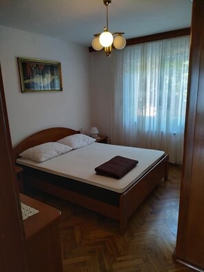 A bedroom with a wooden bed, a nightstand, a lamp, a painting on the wall, and a window with curtains.