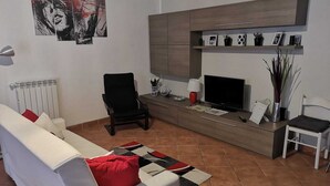 A living room with a white sofa, a black armchair, a TV, and a cabinet with shelves. - Chic 'n Charme Trastevere Terrace (Roma)