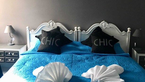 A bed with a blue quilt, two pillows with "CHIC" embroidered, a wall art of a woman with a camera, and a nightstand with a lamp. - Chic 'n Charme Trastevere Terrace (Roma)