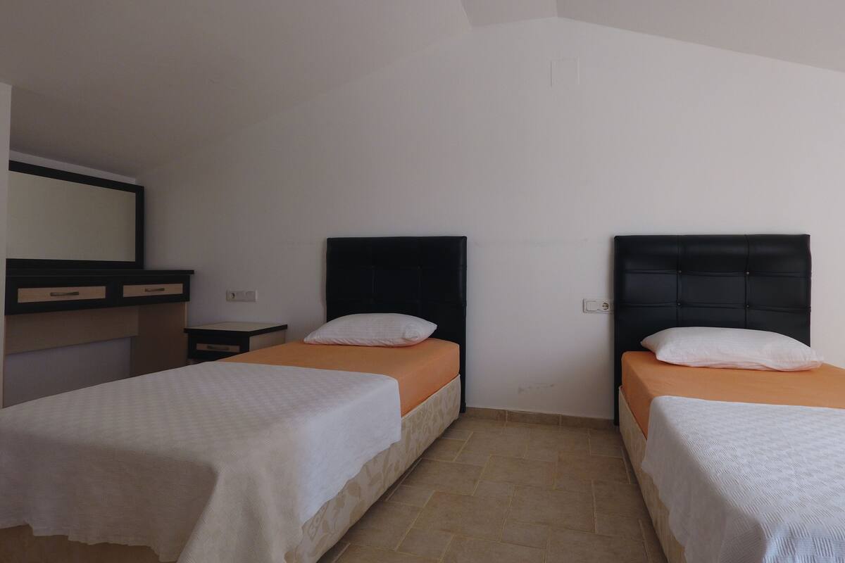 A room with two beds, a small desk, a mirror, and a light switch on the wall.
