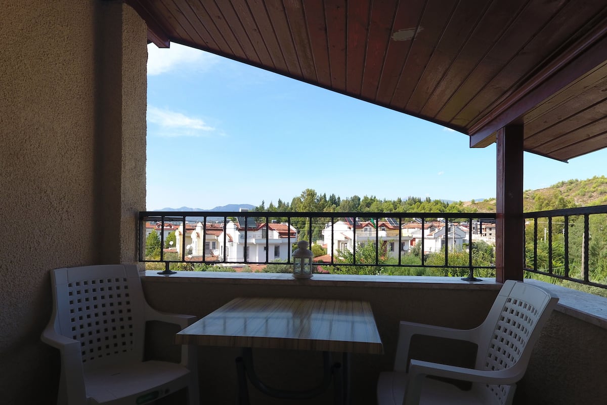 A balcony with a table and two chairs, overlooking a residential area with houses and greenery.