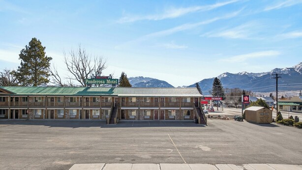 A motel with a green sign, a Texaco gas station, and mountains in the background. - The Ponderosa Motel (Enterprise)