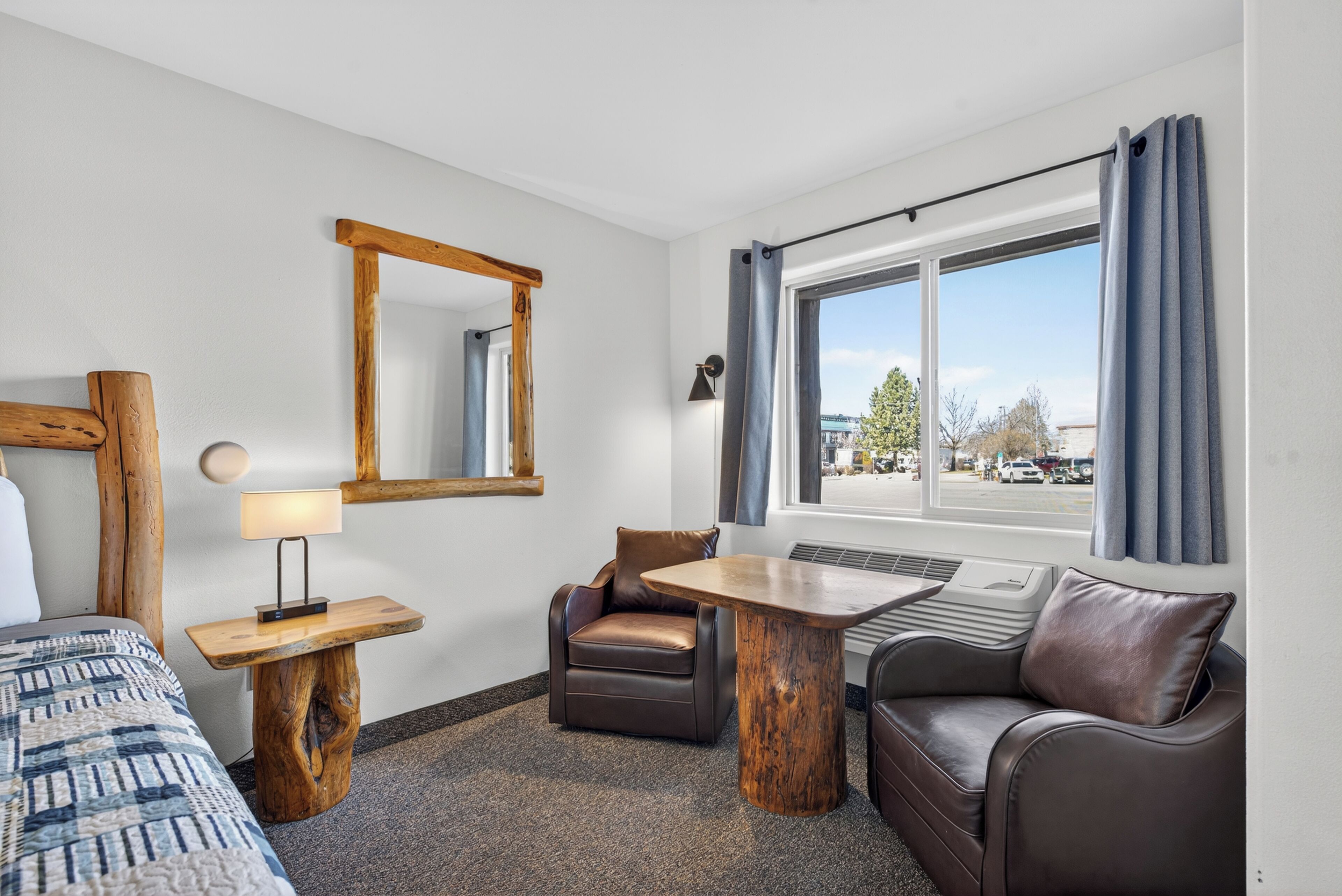 Een hotelkamer met een bed, een bureau met een lamp, een stoel, een bank, een raam met gordijnen en een spiegel aan de muur.