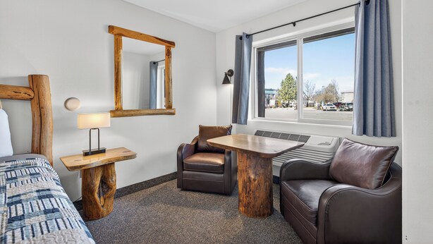 A hotel room with a bed, a desk with a lamp, a chair, a sofa, a window with curtains, and a mirror on the wall. - The Ponderosa Motel (Enterprise)