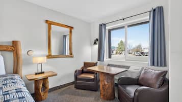 A hotel room with a bed, a desk with a lamp, a chair, a sofa, a window with curtains, and a mirror on the wall.