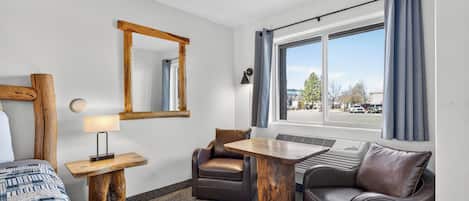 Een hotelkamer met een bed, een bureau met een lamp, een stoel, een bank, een raam met gordijnen en een spiegel aan de muur.