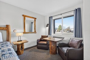 A hotel room with a bed, a desk with a lamp, a chair, a sofa, a window with curtains, and a mirror on the wall. - The Ponderosa Motel (Enterprise)