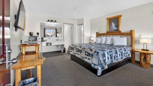 A hotel room with a bed, bedside table, lamp, and a television. - The Ponderosa Motel (Enterprise)