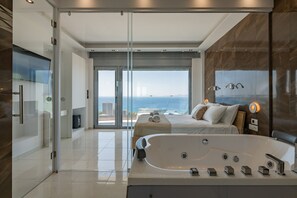 Habitación de hotel moderna con una cama grande, una bañera, cabina de ducha de vidrio y vista al océano.