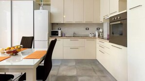 A modern kitchen with white cabinets, a stainless steel oven, a microwave, and a refrigerator. - Apartment Rita (Split)