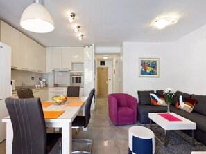 A modern living room with a dining area, kitchen, and a hallway leading to a door. - Apartment Rita (Split)