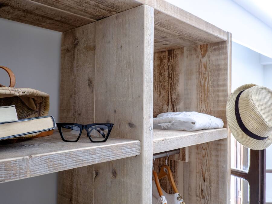 A wooden shelf with books, glasses, and a hat.