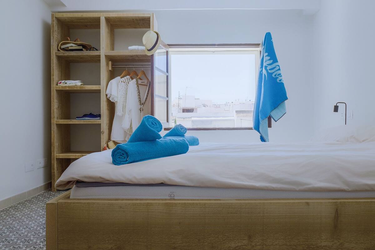A bedroom with a wooden bed, a wardrobe, and a window with a view of buildings.