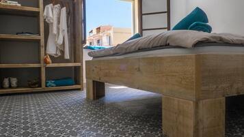 Ein Schlafzimmer mit einem hölzernen Bett, einem Kleiderschrank voller Kleidung und Blick auf Gebäude durch ein Fenster.