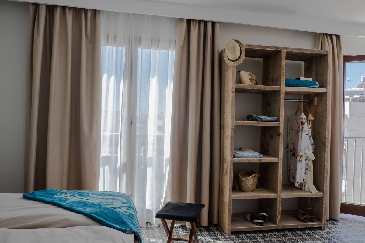 A hotel room with a bed, a wooden wardrobe, and a balcony with a view.