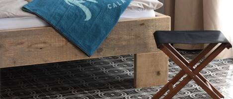 A bed with a blue towel, a wooden nightstand, a black lamp, and a patterned floor.