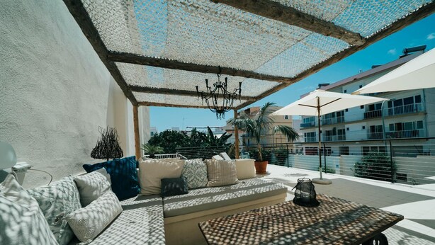 A sunlit outdoor seating area with a sofa, cushions, a table, and a chandelier.