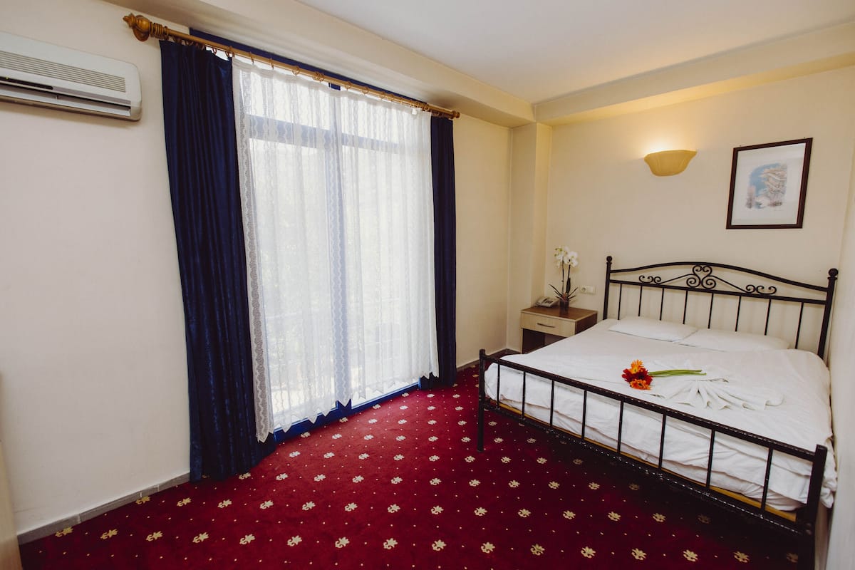 A hotel room with a bed, a nightstand, a lamp, and a window with curtains.