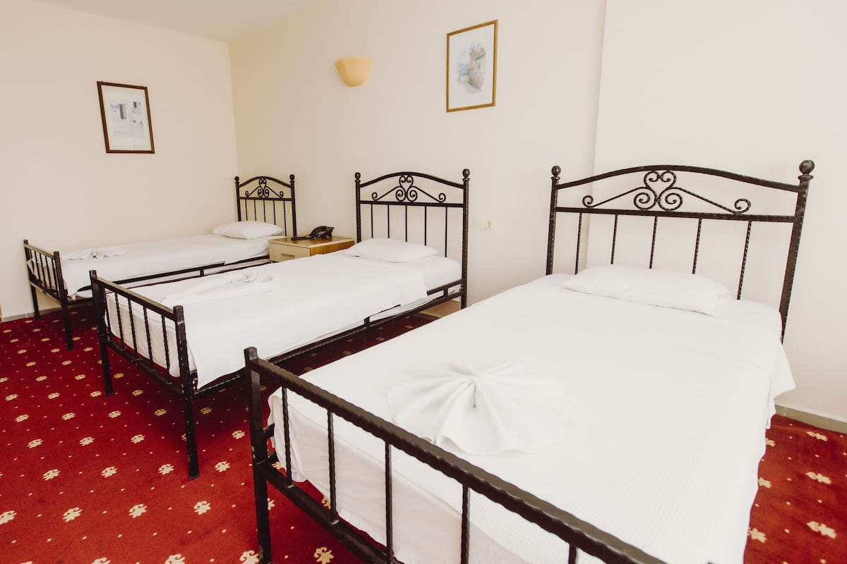 A room with three single beds, a small bedside table with a lamp, and a red carpet with a pattern.