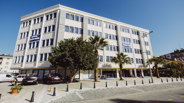 A multi-story hotel with a modern facade, several balconies, and a parking area with cars and a motorcycle. - Ozalp Han Hotel (Ortaca)